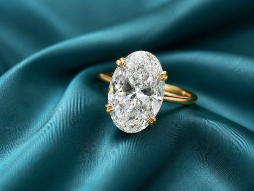 An oval diamond ring with a yellow gold band, resting on draped teal satin fabric.